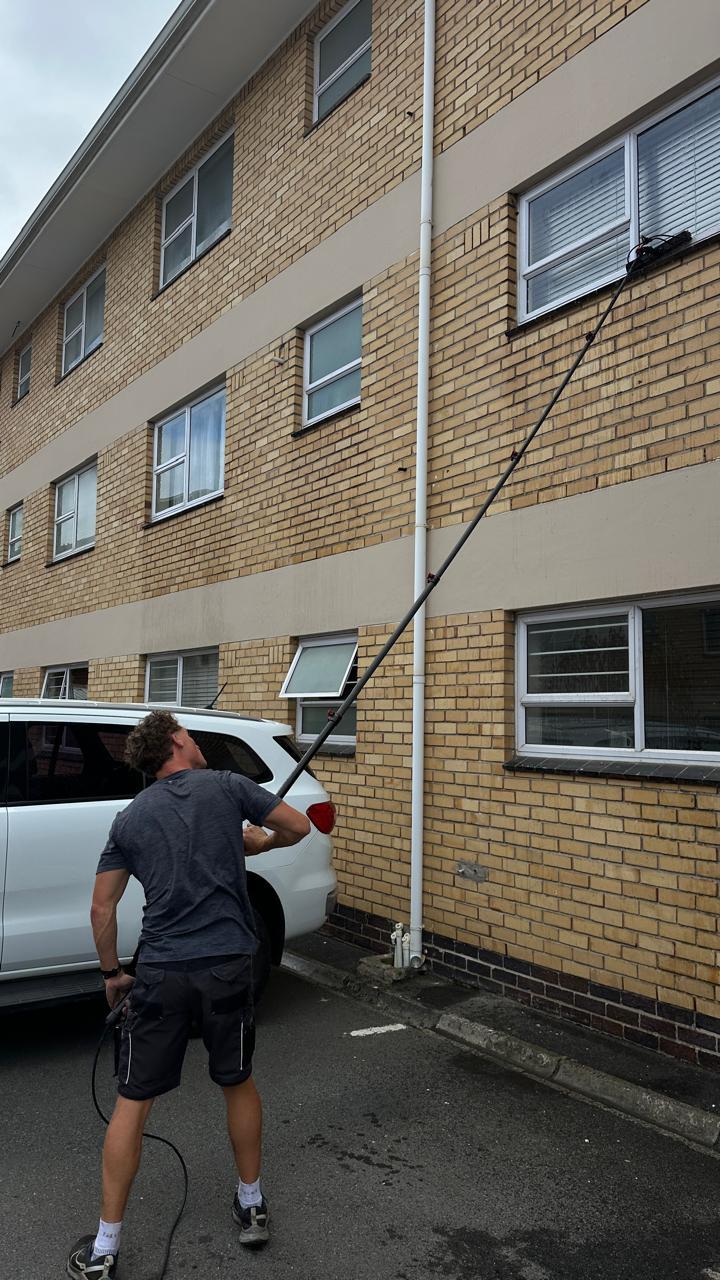 Blu cleaner using a long-reach brush on the upper windows of a brick apartment complex