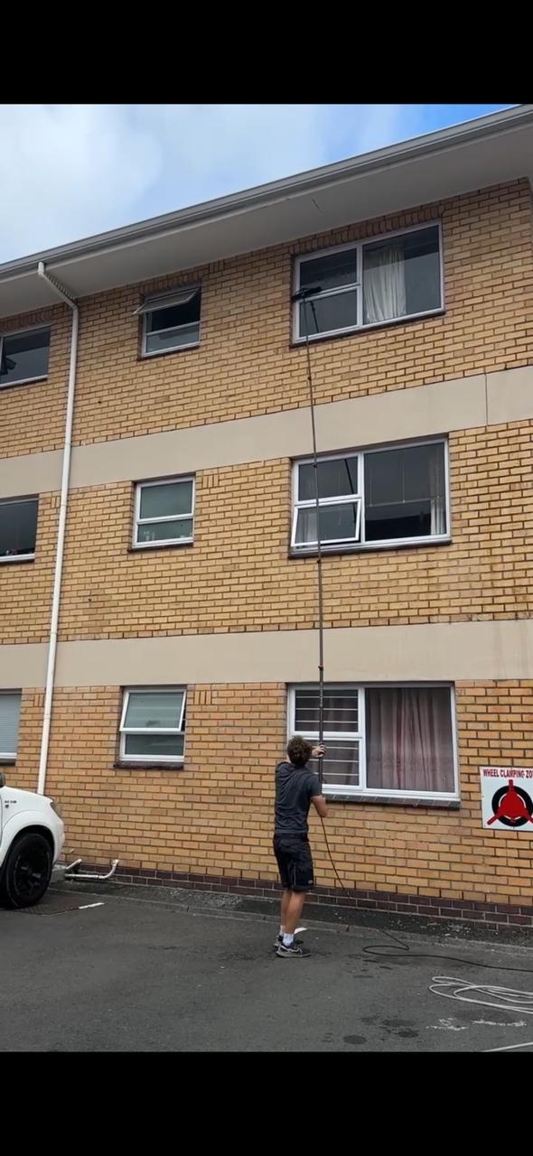 Blu cleaner washing the upper windows of an apartment block from the ground