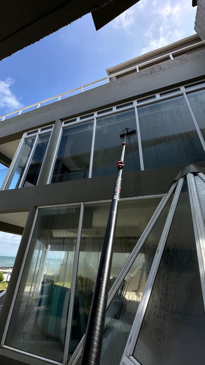 Long-reach brush cleaning large windows on a beachfront building with the sea at the side