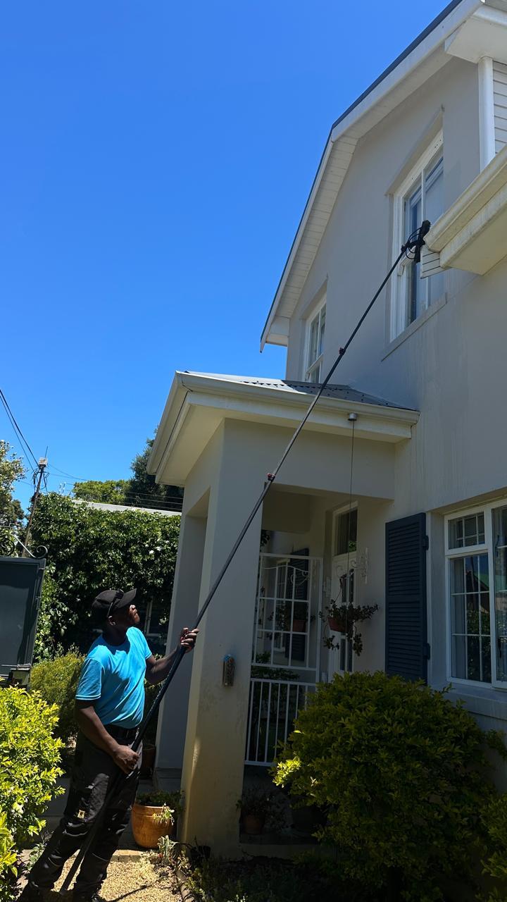 Blu cleaner reaching the upstairs windows of a double-storey Cape Town home with a long-reach brush, standing on the ground