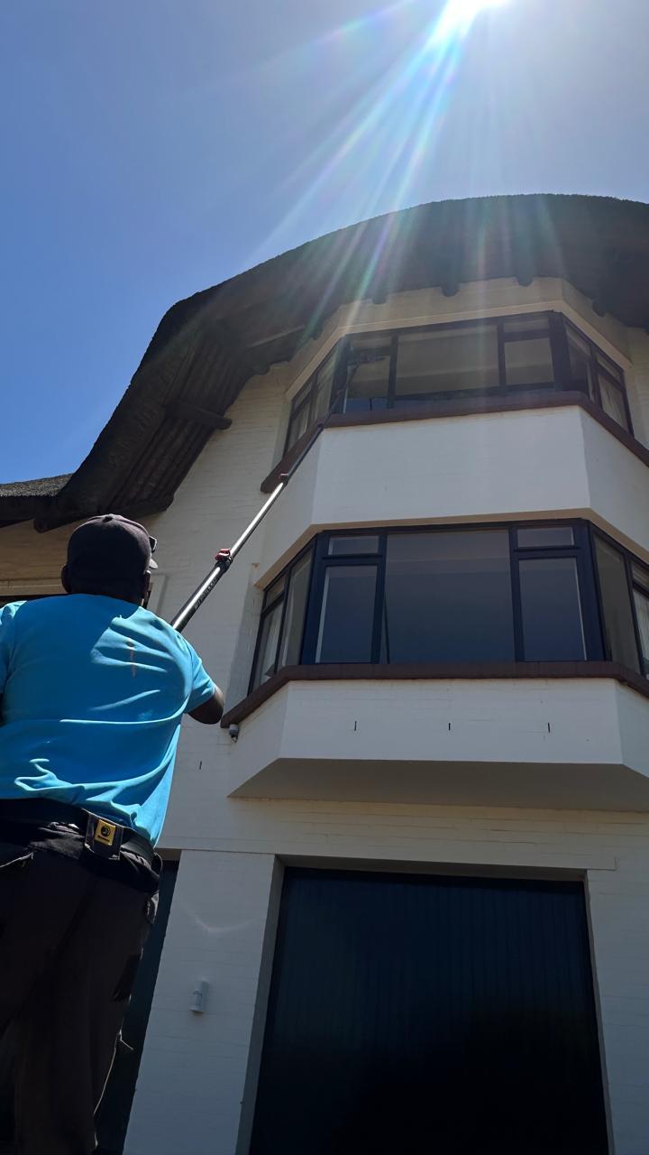 Technician cleaning the upper storey of a curved-front Cape Town house in bright sunlight