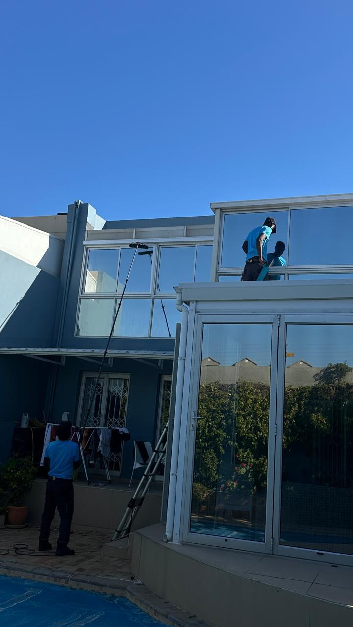 Blu cleaners washing the upper windows of a double storey home beside a pool