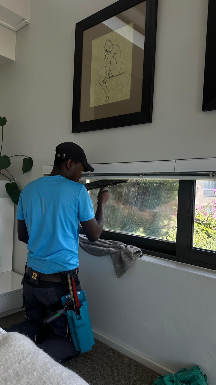 Blu cleaner wiping a window frame and sill indoors with a cloth