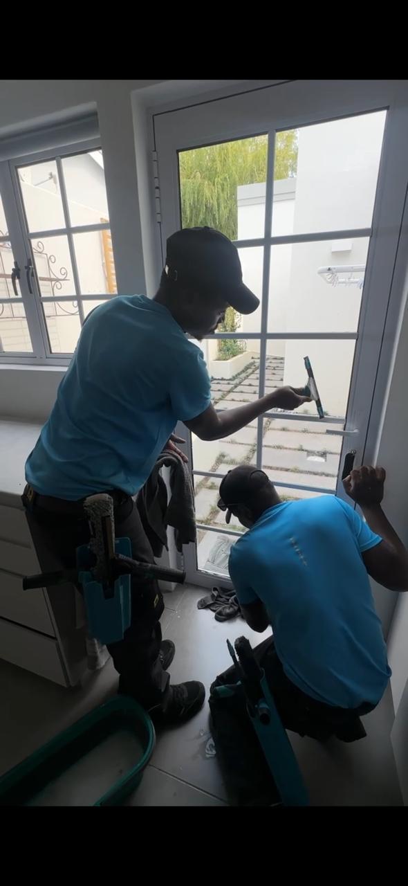Two Blu team members cleaning the panes and lower frame of French doors inside a home