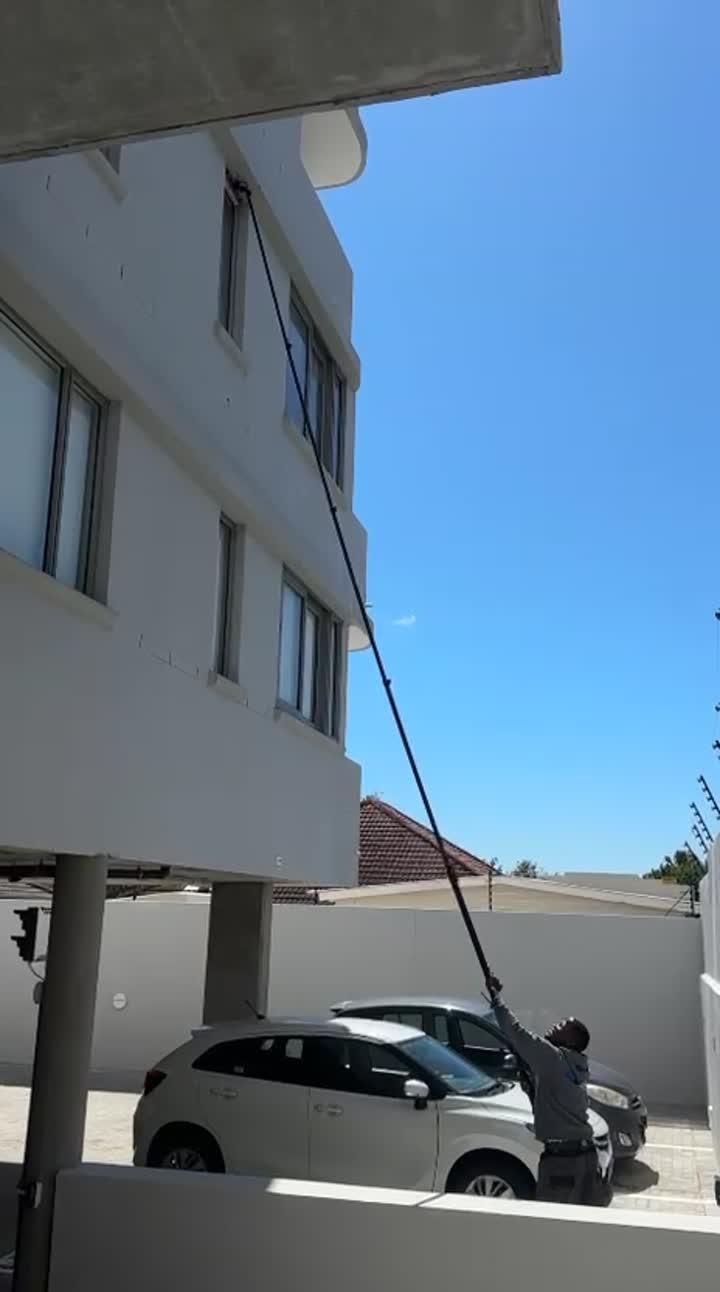 Long-reach brush cleaning the upper windows of a white apartment block