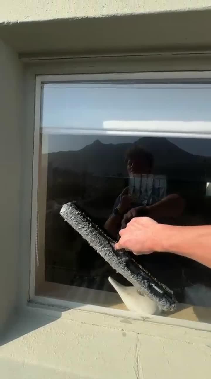 Blu cleaner washing a window by hand with the mountain reflected in the glass