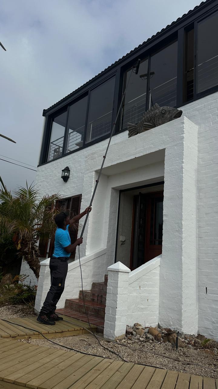 Blu technician cleaning the upper windows of a white double-storey Cape Town home from the ground